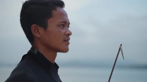 A close up side view of a spear fisherman face holding his speargun and looking out with an out of f