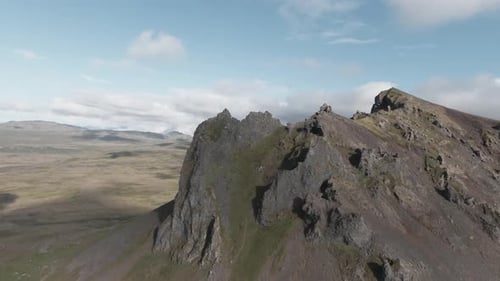 Rocky mountain summit in smooth parallax drone shot, blue sky with clouds