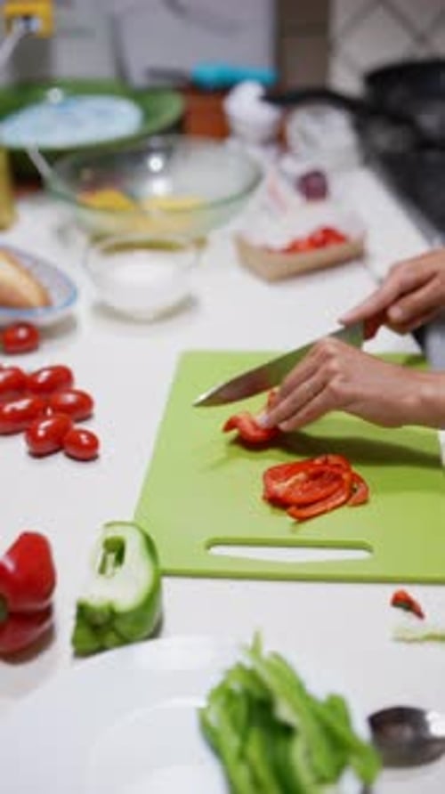 In the Kitchen a Woman is Using a Knife to Slice a Fresh Red Bell Pepper on a Green Cutting Board