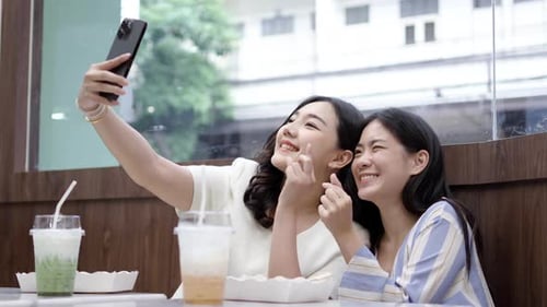 Two young asia females taking selfie using mobile phone while sitting in the cafe