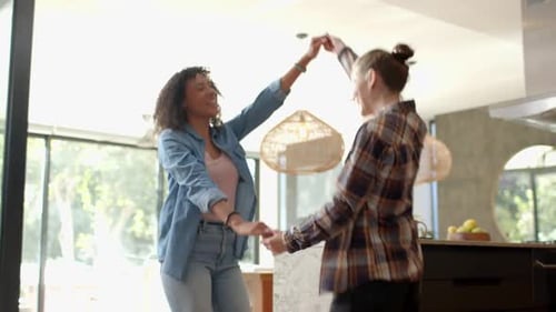 Dancing together, lesbian couple enjoying time in modern kitchen at home