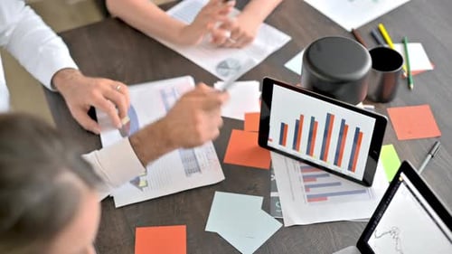 Three people are working and talking in the office. Gadgets and papers with graphs and information