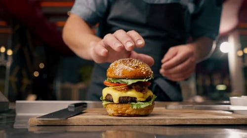 Close-up of a chef pinning a burger with beef patty with vegetables and cheese cooked in the kitchen
