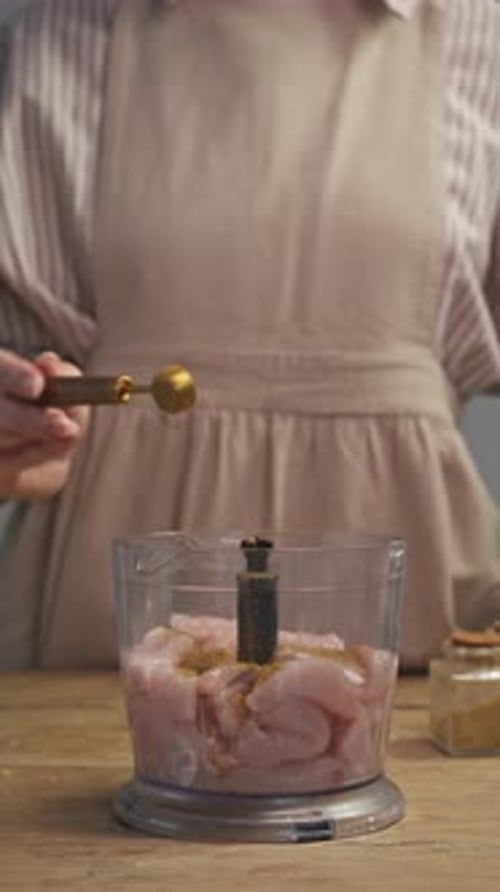 A dona de casa está na cozinha prestes a cortar um pouco de carne de frango no liquidificador. Ela adiciona algumas ervas secas em pó