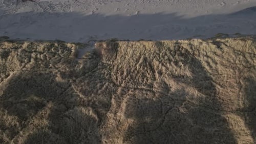 Ridge of sandy dunes leading towards ocean beach, aerial top down shot