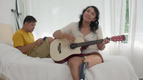 Woman Plays Guitar for Companion on Bed
