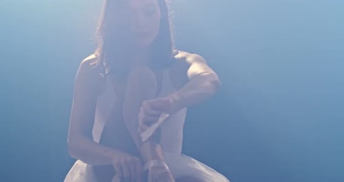 Ballerina Tying Ballet Shoes on the Floor