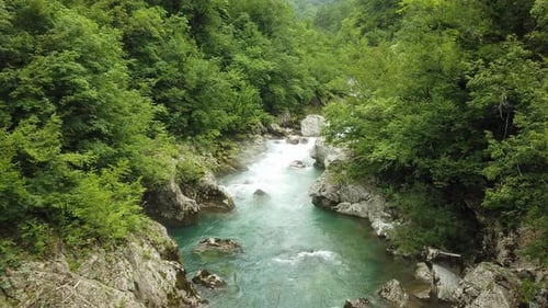 A Turquoise Mountain River Flows Over Rocks the Banks are Covered with Dense Green Forest