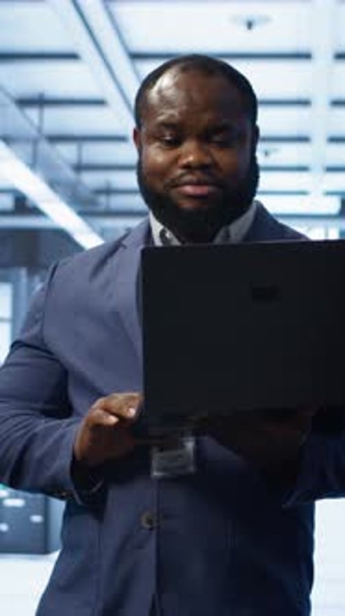 Vertical Video IT Engineer Working on Laptop in Data Center Overseeing Server Operations