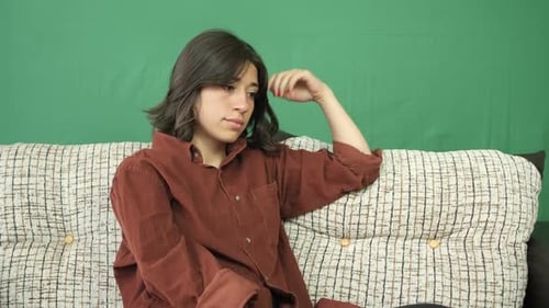 Woman Sitting on Couch, Looking Thoughtful
