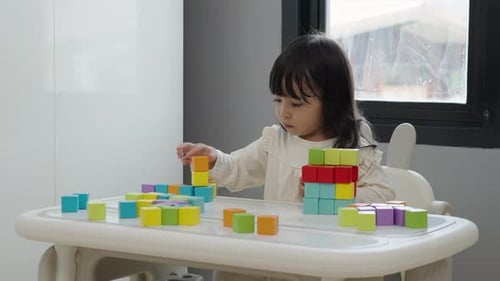 kleines Mädchen spielt Blockspielzeug, um Bauwürfel auf einem Tisch zu stapeln