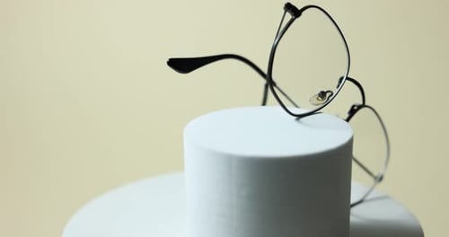 Pair of stylish eyeglasses on podium against light background, rotating