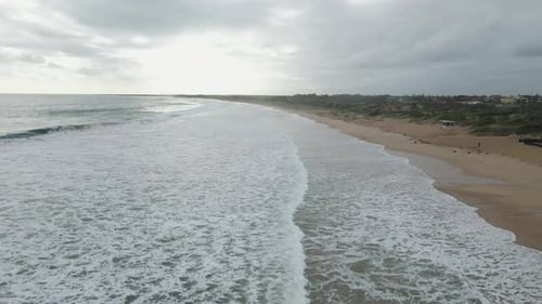 A dynamic high angle shot moving along the shoreline with long waves of water with a lot of sea foam
