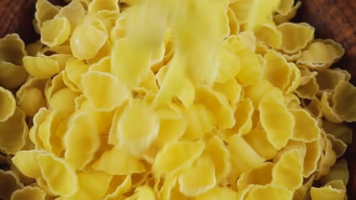 Shell-shaped pasta is poured into a brown ceramic bowl. Top view. Slow motion.