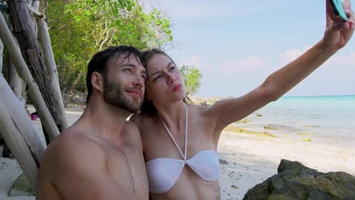 Young couple in Thailand laughing taking photos on beach holiday adventure