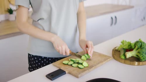 Woman Slices Cucumber for Healthy Salad in Kitchen