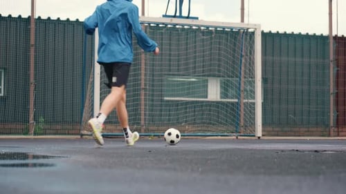 Man Kicks Soccer Ball on Wet Urban Court