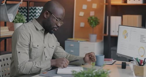 Man Writing in Notebook in Workplace