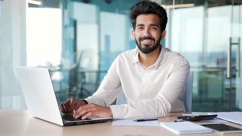 Portrait of a young successful bearded man sitting at a laptop at a workplace in a modern office.