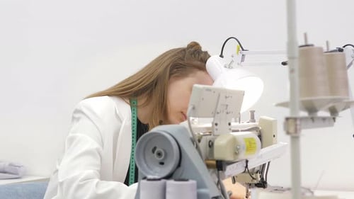 Woman Sews Grey Fabric on a Professional Sewing Machine While Sitting at Her Working Place in