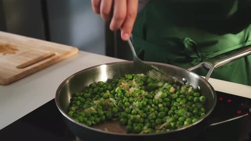 Chef Adding Peas to Onions in Frying Pan