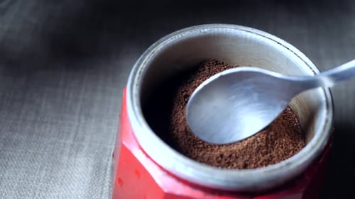 Ralentissement d'une cuillère en aluminium remplissant le compartiment central d'une cafetière italienne rouge