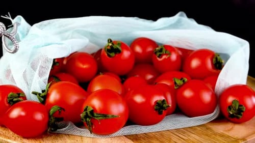 Apila jugosos tomates cherry frescos en una bolsa de malla ecológica que gira suavemente
