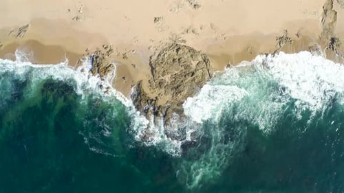 Top aerial drone view of waves crashing on rocky coastline. Blue ocean.