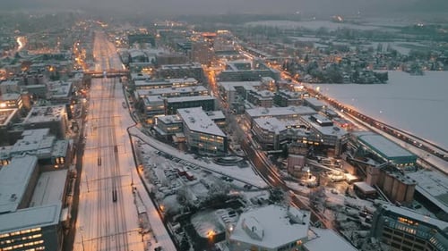 Snowy urban dusk: Aerial view of traffic on city streets lit by evening lights. Captivating winter d