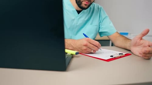 Close-up shot of a male doctor's hand with ring on his finger filling out a patient's history