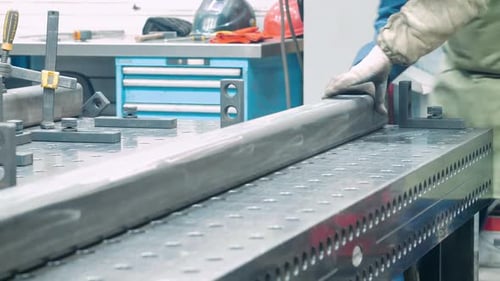 Metalworker Positioning Metal Bar on Perforated Table