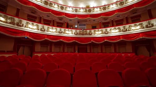 Panoramic view of beautiful richly decorated theater hall. Rows of red chairs in theater hall.