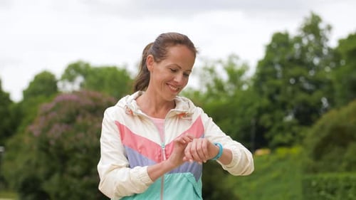 Smiling woman running in park with fitness tracker showcasing sport technology