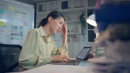 Exhausted Asian young businesswoman overwork late at night in office.