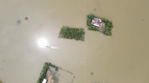 Flooded village in Bangladesh, submerged home with a small boat passing through muddy floodwater