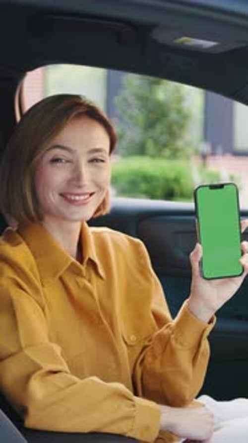 Confident Young Businesswoman in Casual Attire Sitting in a Car Smiling and Holding a Smartphone