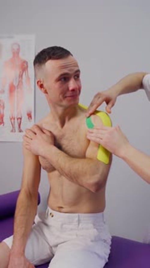 Kinesiology Therapist Applying Kinesiology Tape to a Man's Shoulder Clinic Sports Injury Recovery