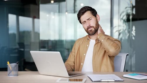 Man Massaging Stiff Neck at Office Desk