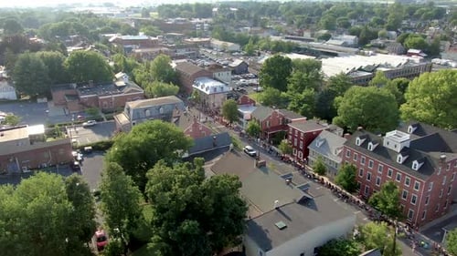 Aerial turn reveals historic town buildings with streets lined with crowds watching Fourth of July p