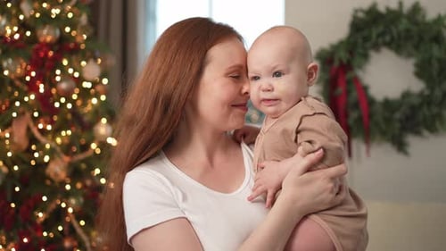 Mother Holding Baby Near Christmas Tree Indoors