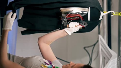 Vertical Video Close Up Professional Dry Cleaning Young Girl Irons a Black Sweater on Hanger with