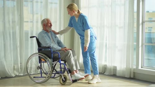 Senior Man in Wheelchair Talks with Young Nurse