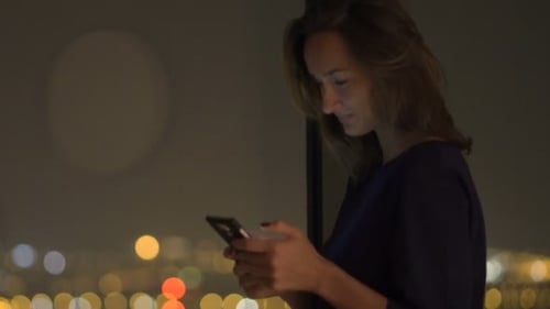 Woman Using Smartphone at Night with City Lights