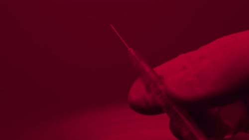 hand in gloves preparing a syringe before the injection , close up in red light emergency room