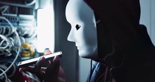 Cyberattaque et pirate masqués avec un smartphone dans une salle de contrôle sombre avec un ransomware pour pare-feu