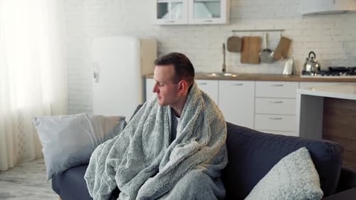 Man Resting on Couch Covered in Blanket