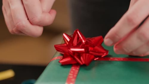Hands Attach Red Bow to Wrapped Gift
