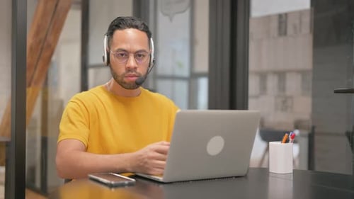 Man Uses Laptop and Headset in Modern Office