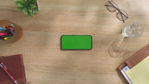 Top down view of a mock up green screen smartphone on a wooden desk
