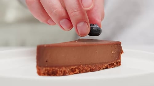 Hand Places Blueberry on Chocolate Cheesecake Slice